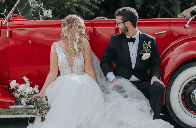 Pareja de esposos posando junto a un carro rojo