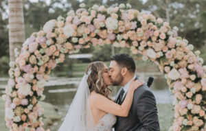 Pareja de novios besándose en su arco de flores durante su boda