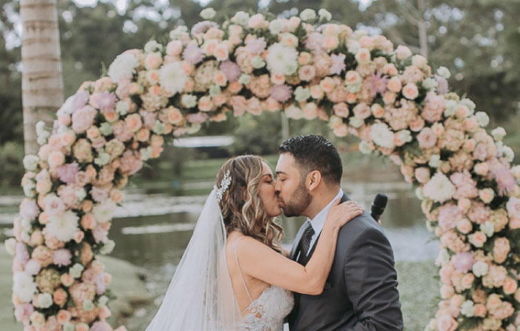 Pareja de novios besándose en su arco de flores durante su boda