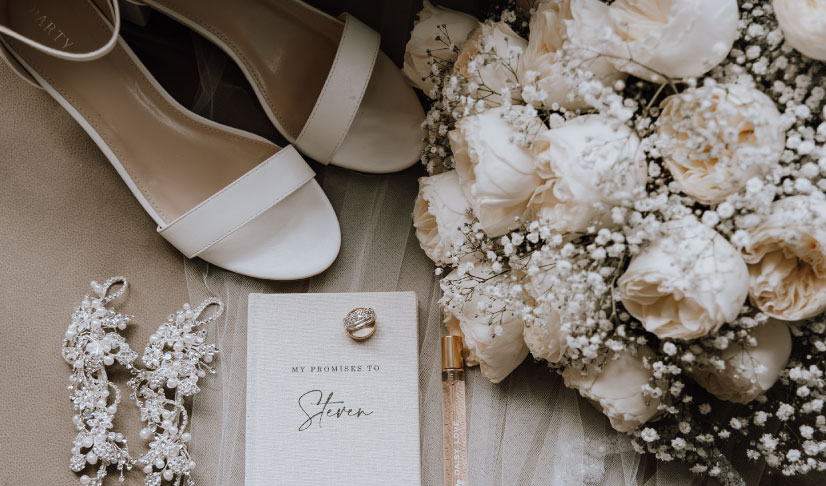 ramo de flores blancas junto a unos zapatos de novia e invitación de matrimonio