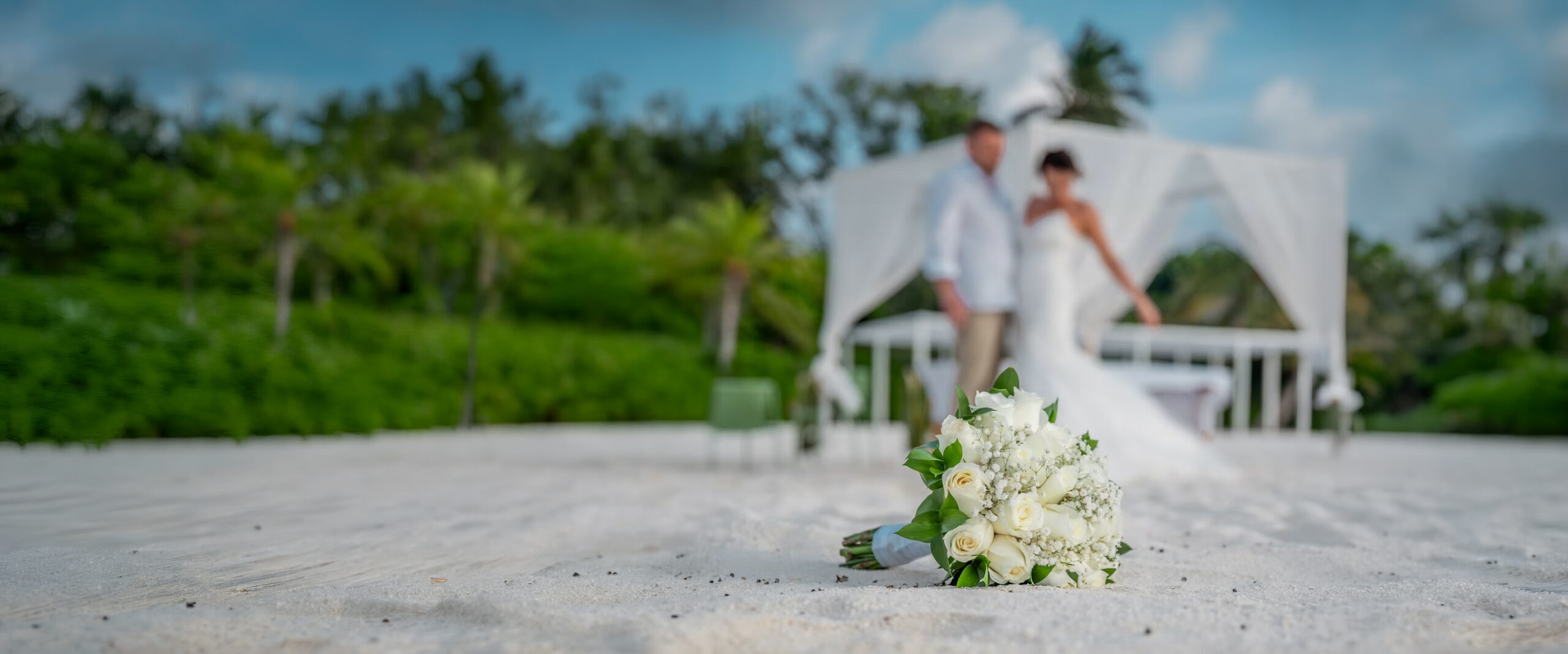 Ceremonia de boda frente al mar bajo una pérgola de telas blancas y flores